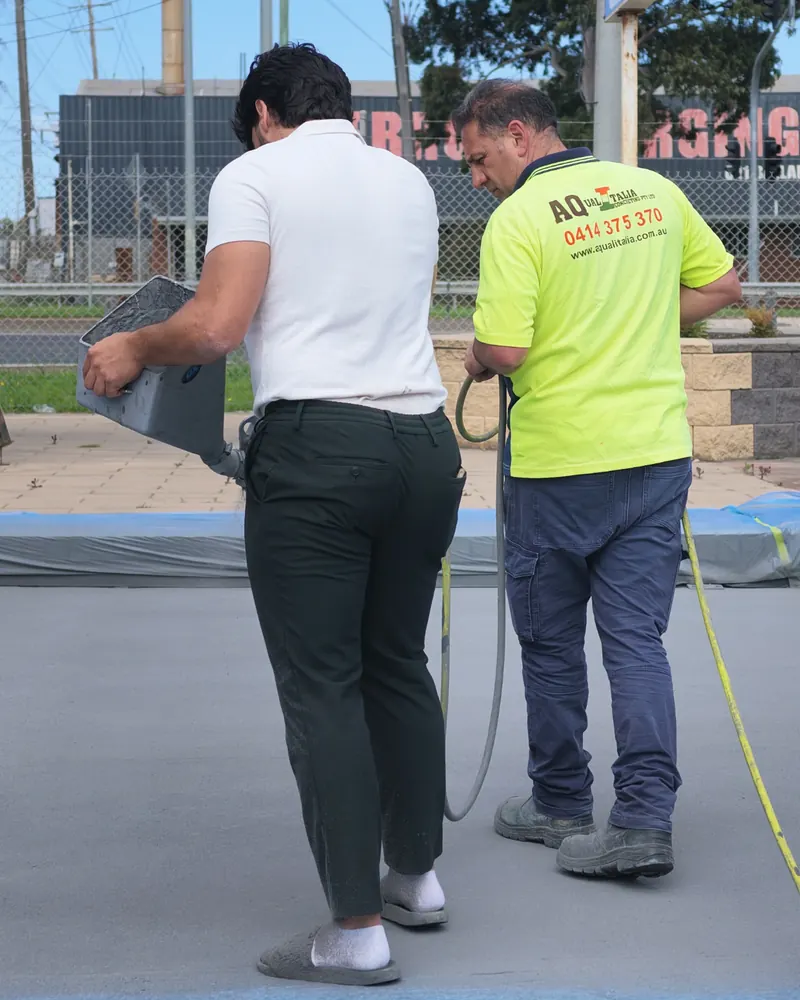 Enrique working beside a student with a hopper gun on a sprayed slab